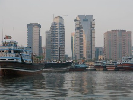 Aircraft between buildings behind dhows on Dubai Creek